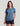 Woman wearing a blue-grey short-sleeve tee with a circular chest pocket graphic, paired with black shorts.