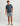 Heather blue t-shirt with circular chest pocket logo, worn with gray shorts and slide sandals.