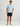 Man wearing light blue short-sleeve t-shirt with small dark logo on chest, black shorts, and gray and white sandals.