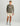 Man wearing olive long-sleeve crew neck shirt with Huk logo, cream shorts, olive baseball cap, and gray water boots.