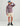 Man wearing mauve hoodie with HUK logo, cream shorts, blue cap, and black boots against neutral background.