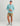 Light blue Huk hoodie with long sleeves and front logo, worn with patterned shorts and gray boots.
