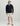 Man wearing navy quarter-zip fleece with small logo, cream shorts, blue and gray cap, and brown sandals.