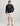 Man wearing black Huk pullover hoodie with gray logo and front pocket, paired with cream shorts.