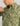 Sage green button-down shirt with abstract print pattern and white buttons, worn by man against neutral background.