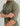 Sage green button-down shirt with chest pocket and icon logo, worn by man with sleeves rolled to elbows.