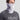 Gray and white camo gaiter worn around neck and lower face, with Huk logo visible on left side.