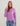 Purple hooded pullover with long sleeves and drawstring hood worn with patterned shorts.