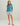 Woman wearing a teal fleece hoodie with long sleeves and blue patterned shorts with front pockets.