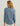 Blue button-up shirt with long sleeves, chest pocket, and curved hem, shown from back view on model.