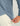 Slate blue oversized shirt with perforated texture and brand logo on chest, worn with cream pants.