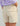 Cream-colored cargo shorts with front and side pockets, shown from behind on a model wearing a lavender top.
