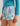 Light blue and white patterned shorts with drawstring waist and HUL logo patch, styled with teal long-sleeve top.