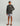 Child wearing charcoal gray long-sleeve hoodie with small logo patch, paired with light gray patterned shorts and sandals.