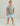 Child wearing gray short-sleeve tee with colorful text graphic and light blue shorts with shark pattern.
