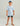 Child wearing light blue short-sleeve t-shirt with blue logo on chest, dark shorts, blue baseball cap, and brown sandals.