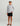 Boy wearing white long-sleeve crew neck shirt with black abstract pattern, black shorts, white and black cap, and brown sanda