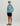 Boy wearing turquoise patterned long-sleeve crew shirt, black shorts, turquoise cap, and brown sandals.