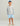 Boy wearing white long-sleeve crew neck shirt with blue logo and text on sleeve, light blue shorts with shark pattern, and bl