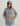 Child wearing gray Huk hoodie with blue logo, hood up, hands in kangaroo pockets, baseball cap visible underneath.